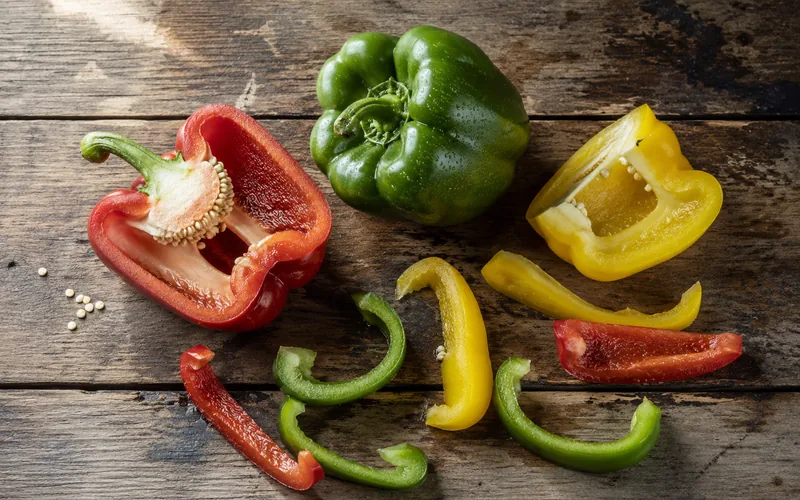 Sliced red, yellow, and green bell peppers arranged on a rustic wooden farm table