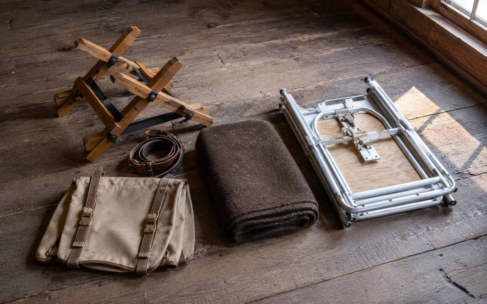 A cross-buck pack saddle with soft panniers laid out next to a collapsible milking stand on a barn floor