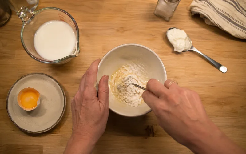 Top-down view of hands mixing emergency kitten formula with goat milk, an egg yolk, and yogurt in a bowl