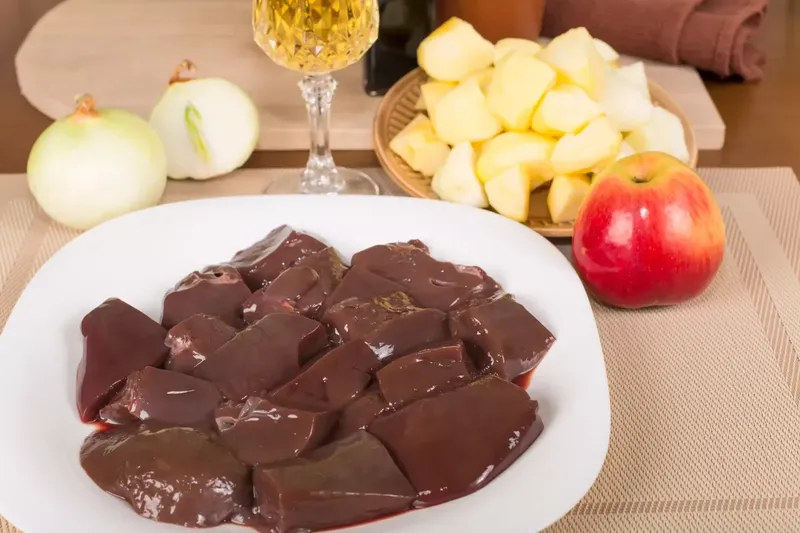 Raw goat liver pieces on a plate with onions and apples ready for cooking