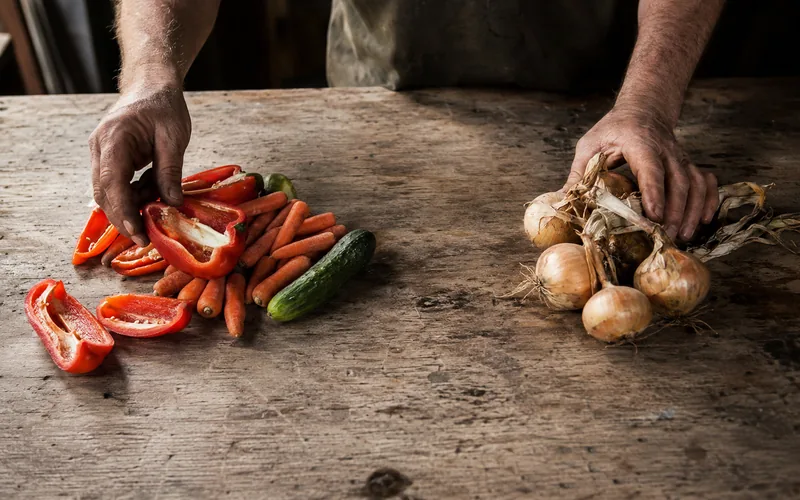 A farmer's hands separating safe goat treats like bell peppers and carrots from vegetables to avoid
