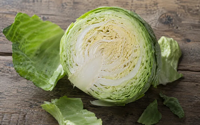 Freshly halved green cabbage head on a rustic wooden surface showing the pale densely layered inner leaves