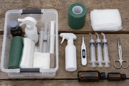 A goat first aid kit laid out on a workbench with wound spray, a thermometer, syringes, and supplements